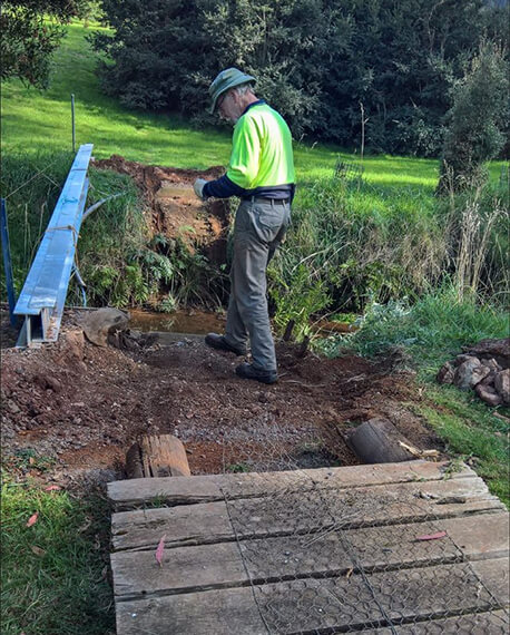 a volunteer in high-vis clothes oversees the replacement of an old wooden bridge
