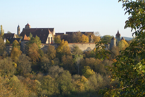 Rothenburg, Germany with a thick forest of trees in front displaying autumn colours.